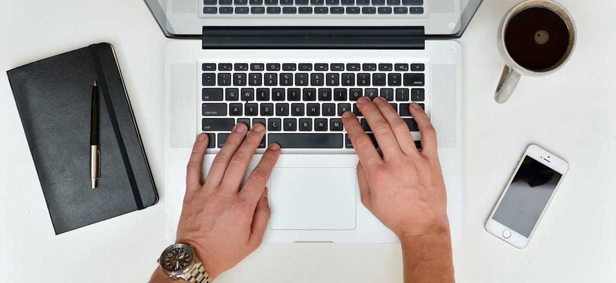 Das Symbolbild zeigt Hände, die auf einem Notebook schreiben. Das Bild zeigt sinnbildlich eine Person, die ihre Website aktualisiert.