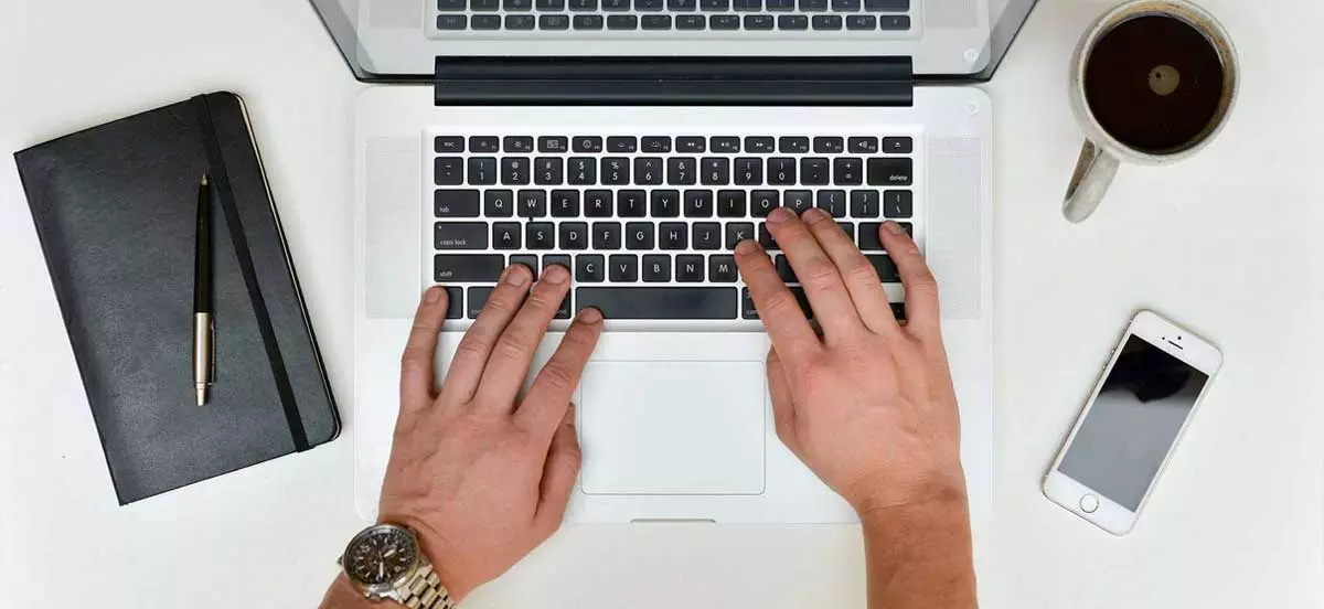Das Symbolbild zeigt Hände, die auf einem Notebook schreiben. Das Bild zeigt sinnbildlich eine Person, die ihre Website aktualisiert.