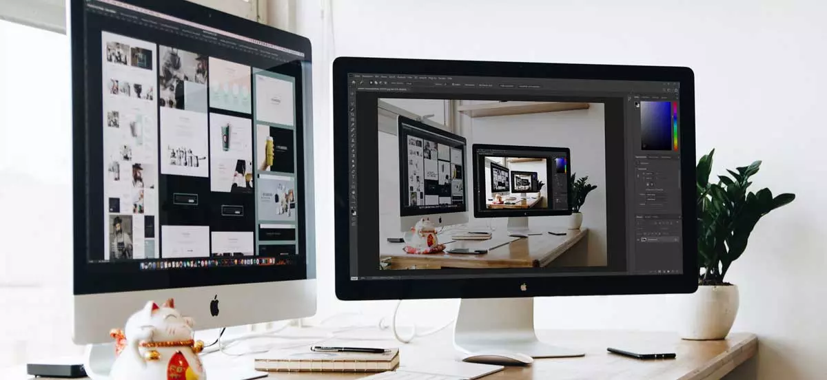 Das Bild zeigt einen Computerarbeitsplatz mit geöffnetem Photoshop auf einem der Bildschirme. Das bild steht für die Verwendung eines Bildbearbeitungsprogramms.